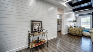 Un salon moderne avec un plancher en bois, un mur recouvert de panneaux blancs, une table basse en bois, un canapé et un ventilateur de plafond.