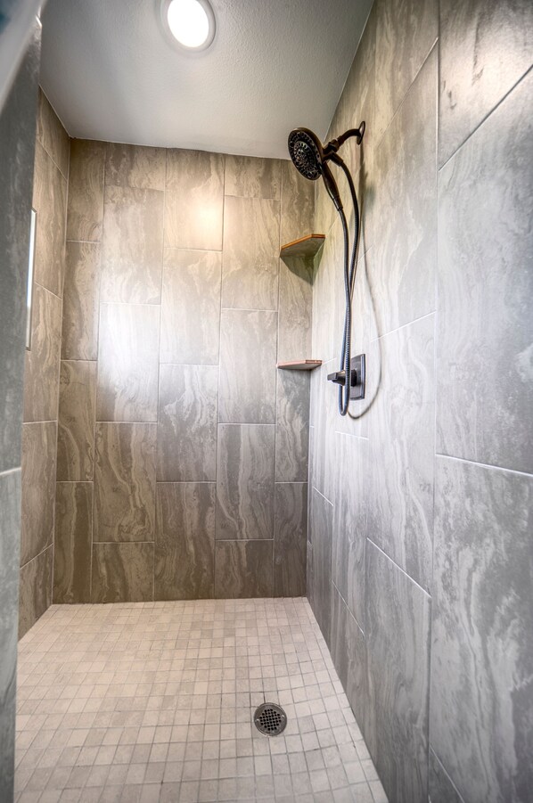 Een douche met een handdouche aan de muur, een klein plankje en een afvoer op de vloer.