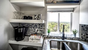 Une cuisine équipée d’une machine à café, de verres à vin et offrant une vue sur l’extérieur.