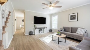 Un salon moderne avec un canapé gris, une table basse, un téléviseur fixé au mur et un escalier avec des éléments en bois.