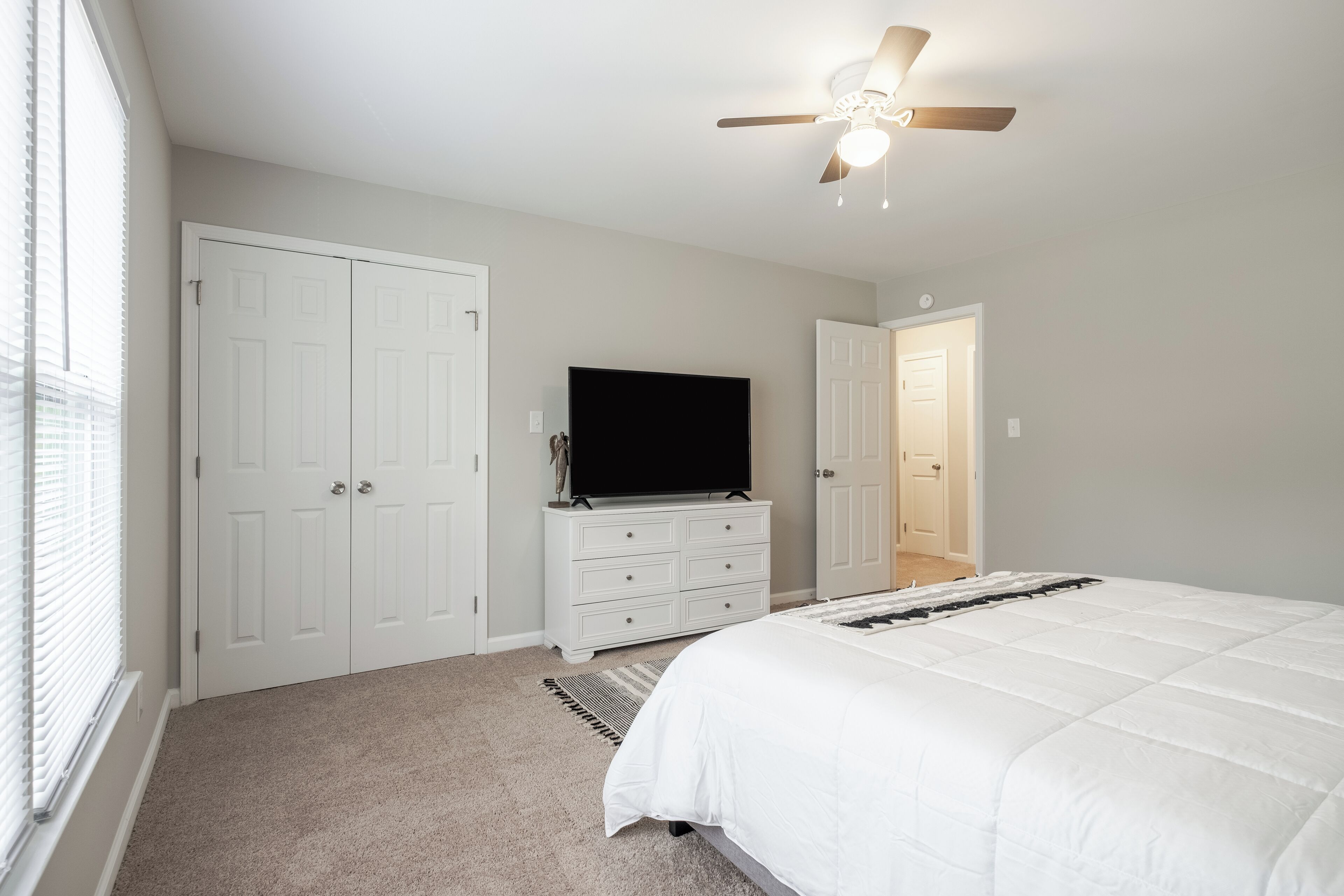Une chambre à coucher comprenant un lit, une commode, un téléviseur et un ventilateur de plafond.