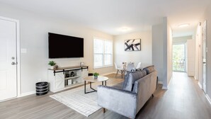 Ett modernt vardagsrum med en platt-TV, en soffa, ett matbord och en köksdel.
