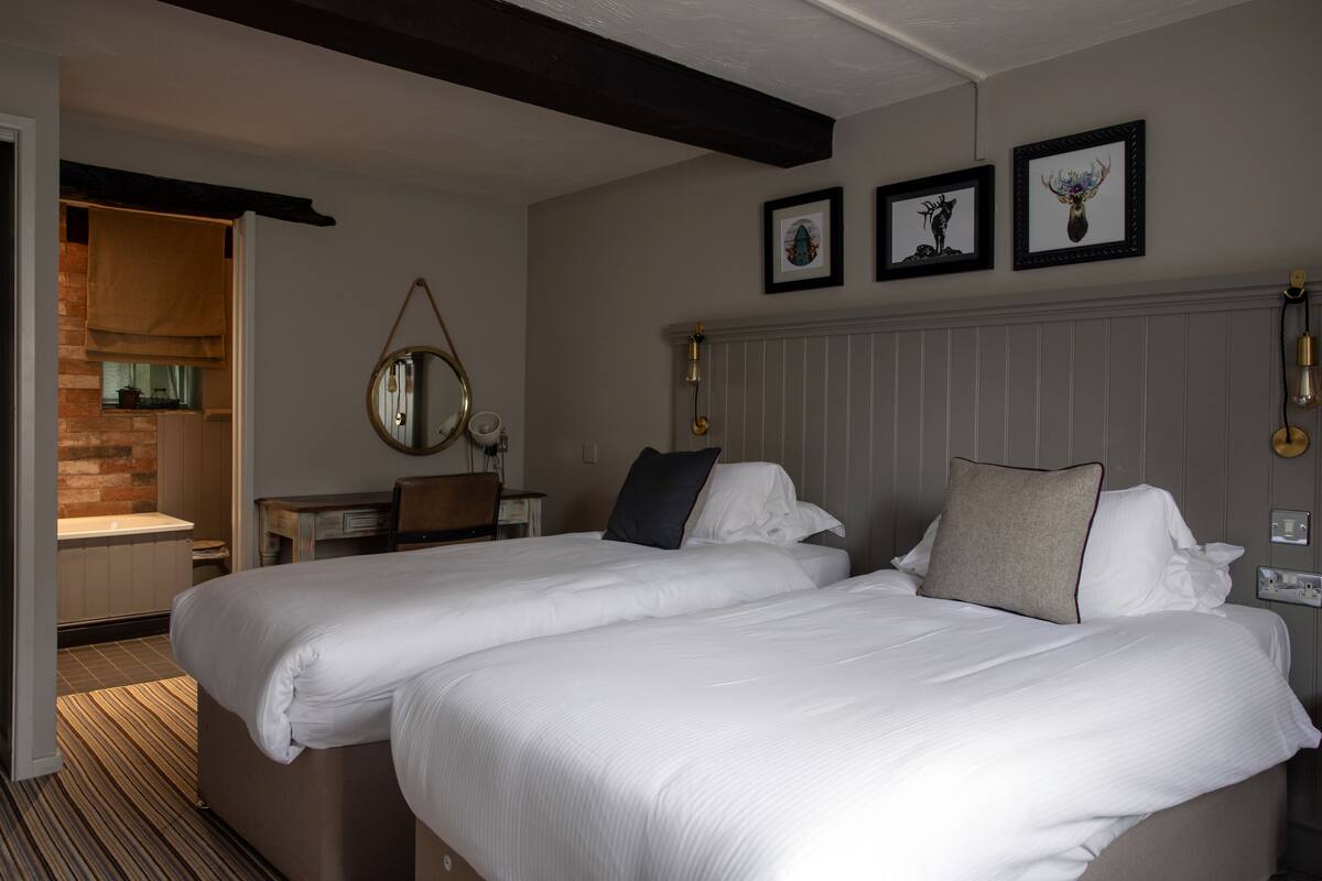 Habitación de hotel con dos camas, un escritorio de madera, un espejo y obras de arte enmarcadas en la pared.