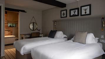 A hotel room with two beds, a wooden desk, a mirror, and framed artwork on the wall.