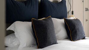 A neatly made bed with white linens and two decorative pillows, a headboard with three framed deer silhouettes, and a wall-mounted light fixture. - The White Hart (Chippenham)