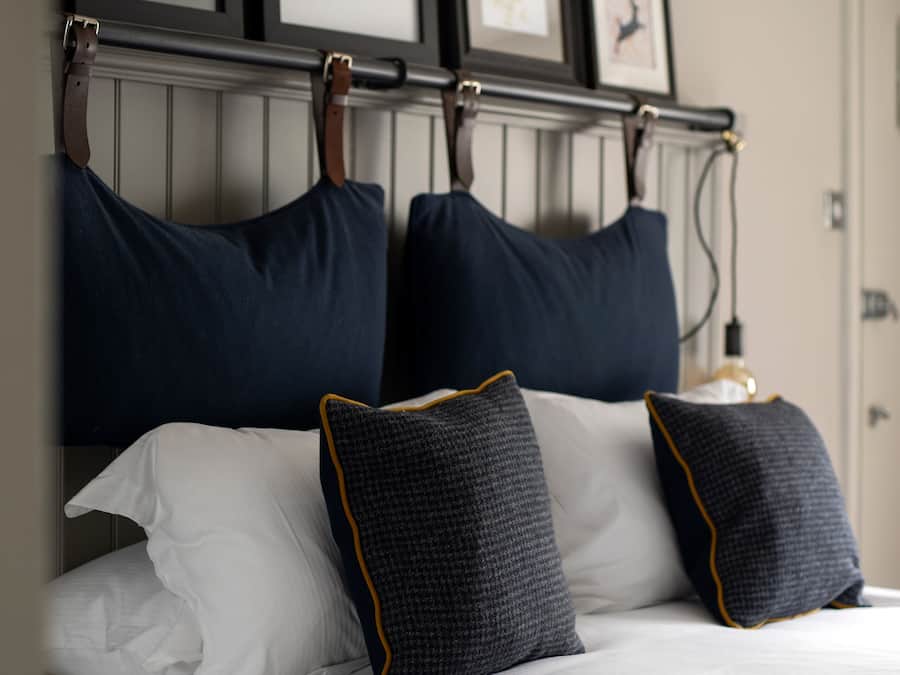 A neatly made bed with white linens and two decorative pillows, a headboard with three framed deer silhouettes, and a wall-mounted light fixture.