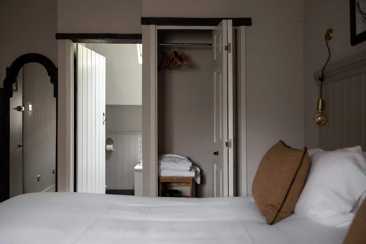 Un dormitorio con una cama, un banco de madera y un armario con ropa colgada.