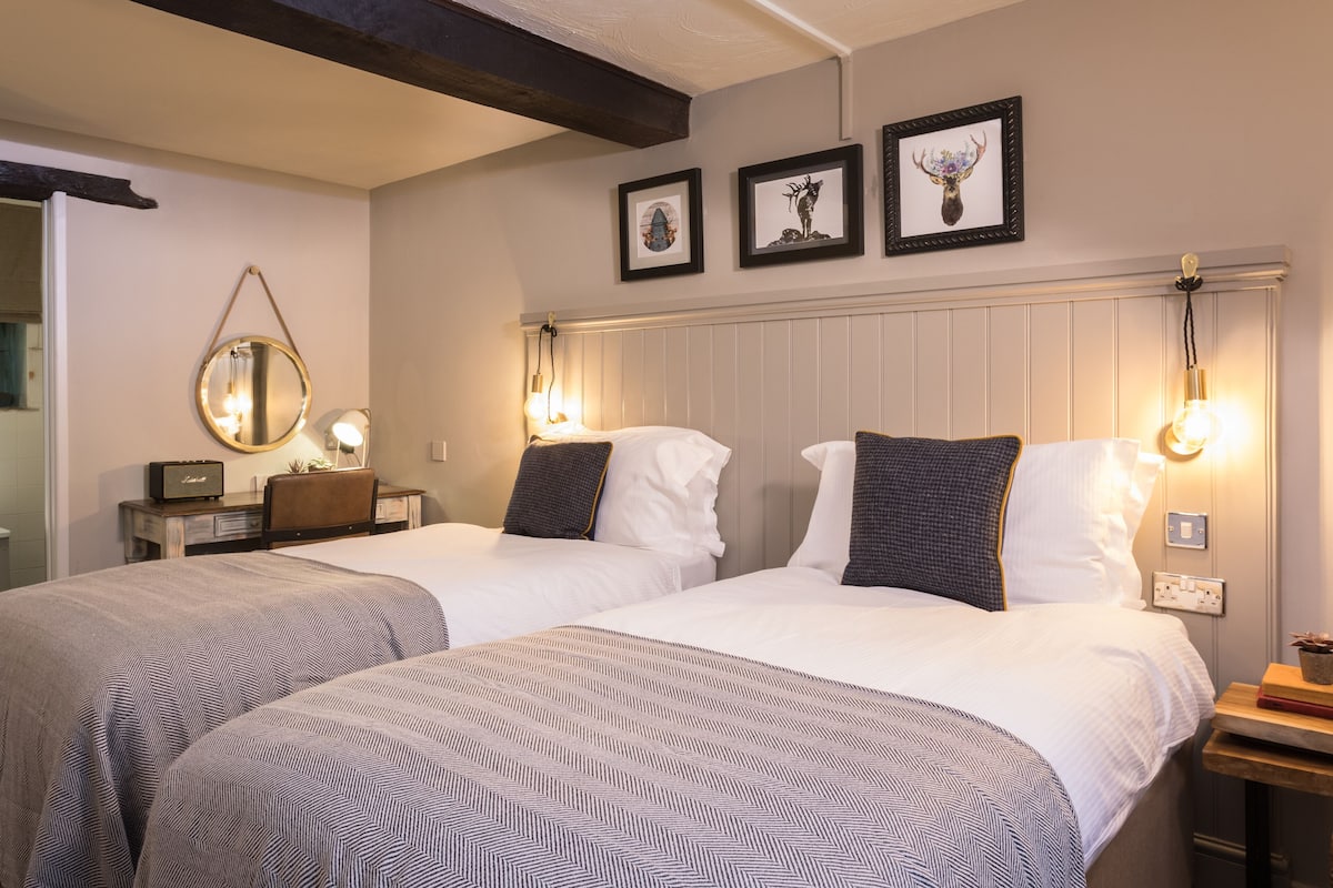 Habitación de hotel con dos camas, una mesita de noche, un espejo y cuadros en la pared.