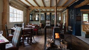 A rustic interior with wooden beams, a fireplace, and a dining area with chairs and tables. - The White Hart (Chippenham)