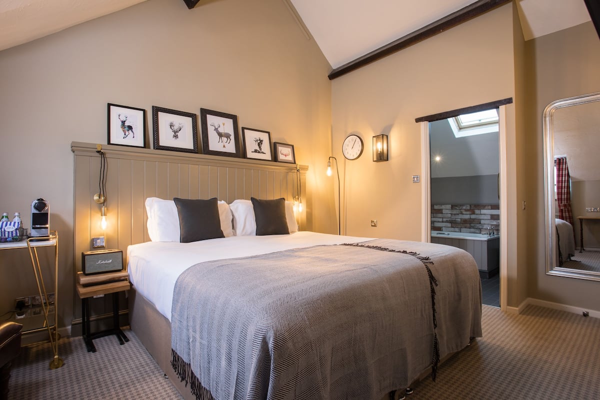 Habitación de hotel con cama, mesitas de noche, un reloj, cuadros en la pared y vistas al exterior.