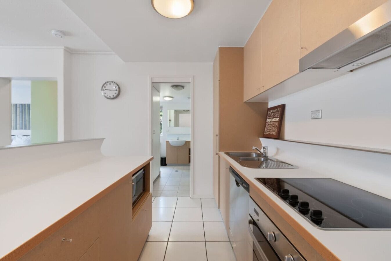 A modern kitchen with white countertops, wooden cabinets, a built-in oven, and a stainless steel sink.