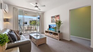 Ein modernes Wohnzimmer mit einer Ledersofa, einem Glastisch, einem Holz-TV-Möbel und einem Deckenventilator.