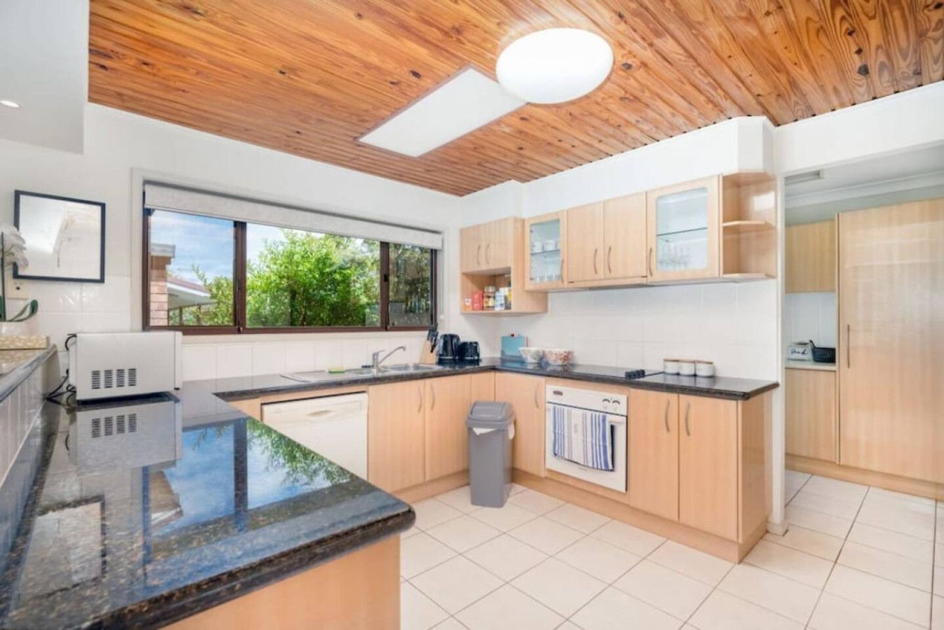 A modern kitchen with wooden cabinets, a black countertop, and a window providing a view of greenery outside.