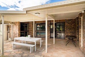 A covered patio area with a white table and bench, brick walls, and large windows.