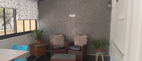 A small, cozy room with a dining table, two wicker chairs, a small side table, and a potted plant.