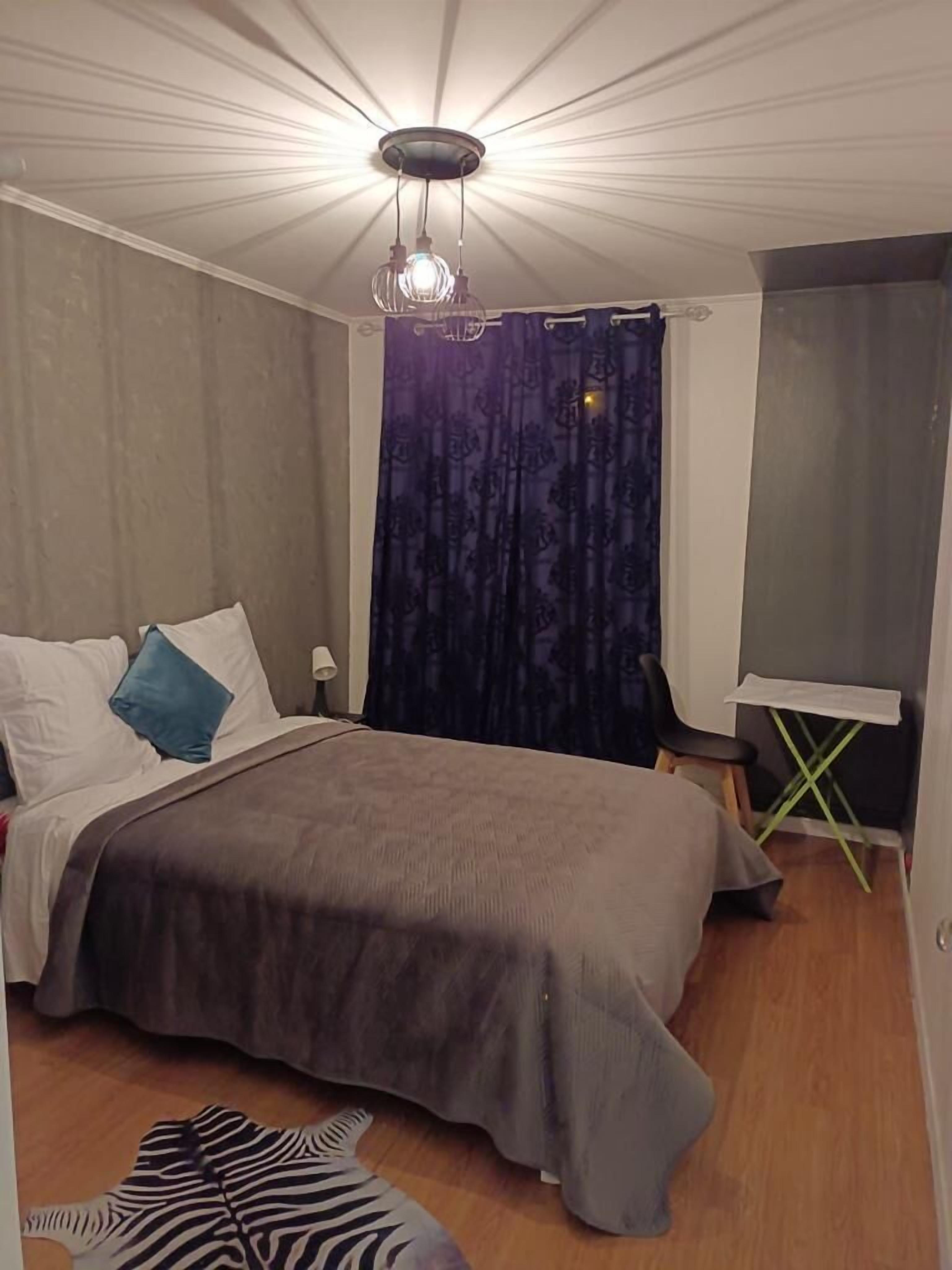A bedroom with a bed, a chair, a small table, and a zebra-patterned rug.