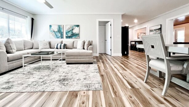 A modern living room with a sofa, ottoman, coffee table, and a dining area with a chair and table.