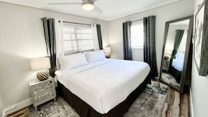 A bedroom with a bed, a ceiling fan, a nightstand with a lamp, and a large mirror.