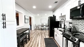 A modern kitchen with white cabinetry, a black stove, and a dining area with a bench.