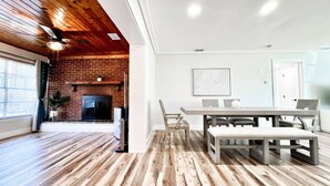 A spacious living room with a wooden floor, a fireplace, and a dining area with a table and chairs.