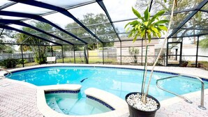 A covered swimming pool with a hot tub, surrounded by a paved patio and a metal fence.