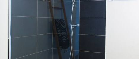 Zona de ducha con paredes de vidrio, suelo de azulejos y una escalera apoyada en la pared.