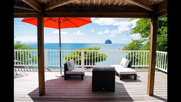 A covered deck with a view of the ocean, featuring two lounge chairs and a red umbrella. - Alexandra TURQUOISE (Le Diamant)