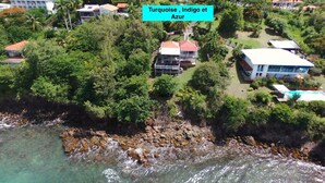 An aerial view of a coastal property with multiple buildings, lush greenery, and a rocky shoreline. - Alexandra TURQUOISE (Le Diamant)