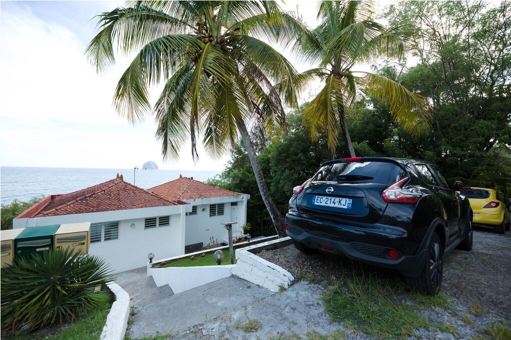 Une maison située sur la côte, avec un toit recouvert de tuiles rouges, une voiture noire garée devant et une voiture jaune à côté.