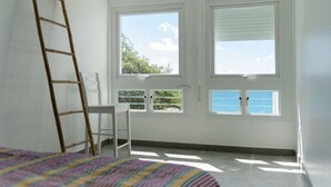 A room with a bed, a ladder, a chair, and large windows with a view of the sea. - Alexandra TURQUOISE (Le Diamant)
