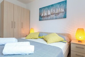 A bedroom with a bed, pillows, a nightstand, a lamp, a painting, and a wardrobe.