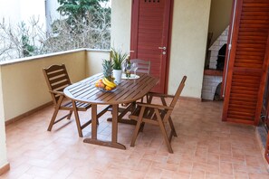A wooden table with chairs, a potted plant, and a fruit bowl on a tiled balcony.