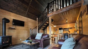 A cozy cabin interior with a wooden interior, a fireplace, leather sofas, a dining table, and a kitchen area. - Luxury Stargazer Cottage - Joby Chungo  (Nordegg)