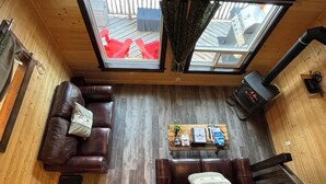 A cozy room with a wooden floor, two leather sofas, a coffee table with books, a fireplace, and a skylight. - Luxury Stargazer Cottage - Joby Chungo  (Nordegg)