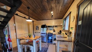 A compact kitchen with wooden walls and a central island, equipped with a stove, sink, and refrigerator. - Luxury Stargazer Cottage - Joby Chungo  (Nordegg)
