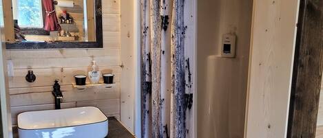 Ein rustikales Badezimmer mit einem Holzwaschbecken, einem Spiegel und einer Dusche mit einer Holztür.