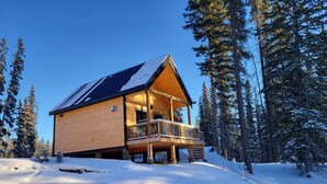 A wooden cabin with a balcony, surrounded by snow-covered trees. - Luxury Stargazer Cottage - Joby Chungo  (Nordegg)
