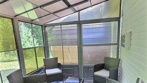 Un patio couvert aménagé avec des meubles en osier et une table à plateau en verre.