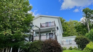 Une maison à deux étages dotée d’un balcon, entourée d’une végétation luxuriante et d’une pelouse bien entretenue.