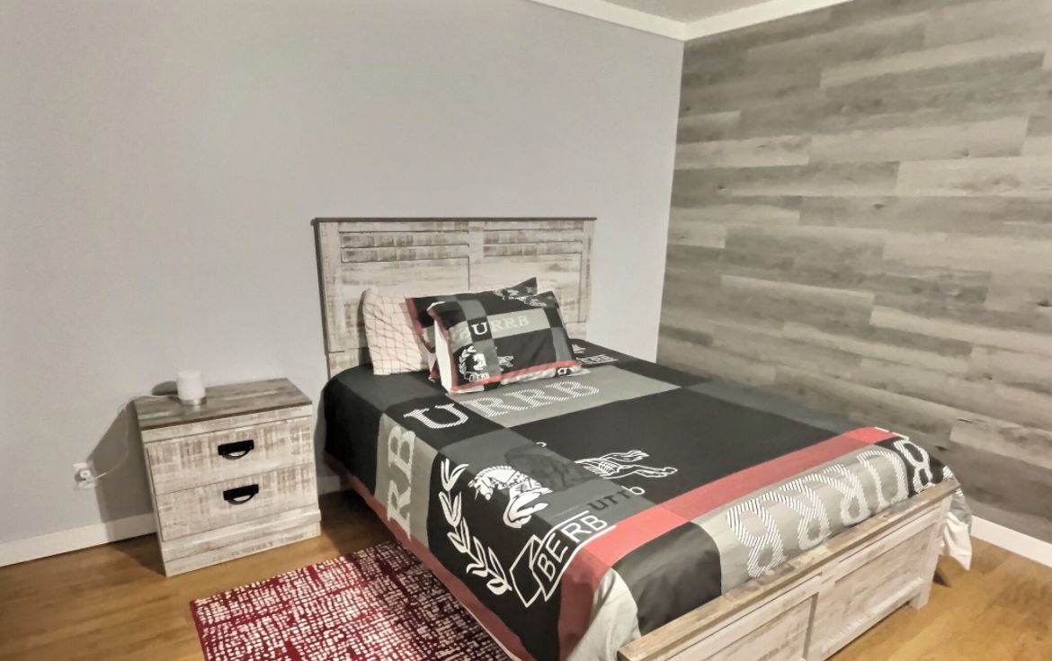 Ein Schlafzimmer mit einem Bett, einem Nachttisch, einem roten Teppich mit Muster und einer Holzwand.