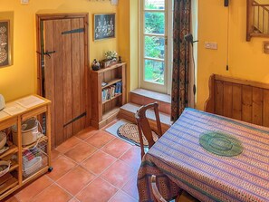 A room with a wooden door, a bookshelf, a window with curtains, a table with a patterned tablecloth, and a chair. - 1 bedroom accommodation in Ashbourne (Ashbourne)