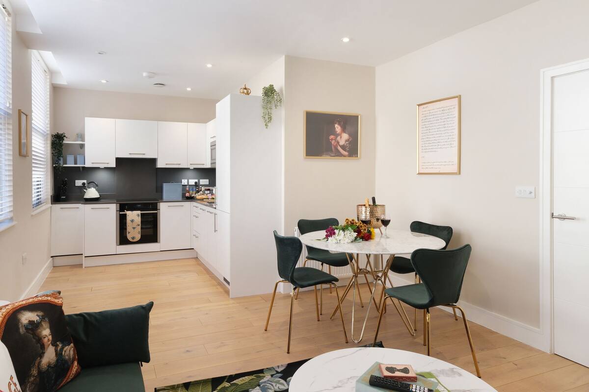 Una sala moderna con una mesa de comedor, sillas verdes, un sofá y una cocina al fondo.