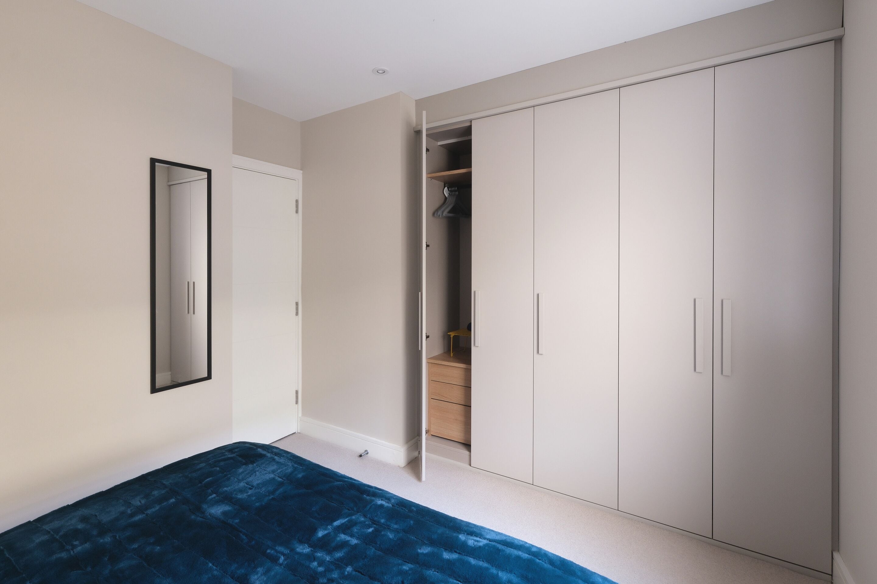 A bedroom with a large wardrobe, a bed with a blue cover, and a mirror on the wall.