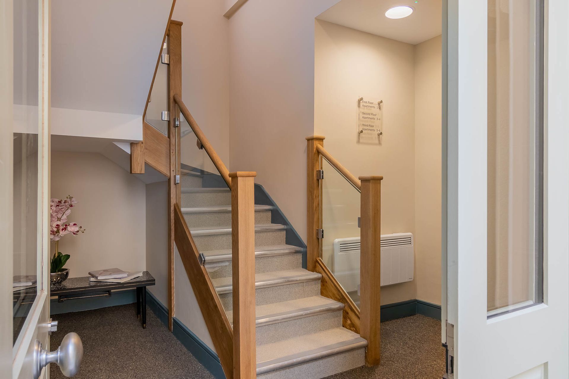 A staircase with wooden railings and carpeted steps, leading to an apartment.