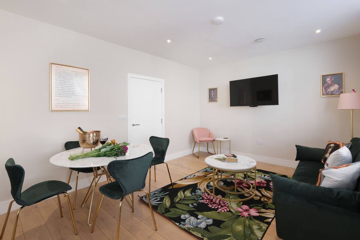 Una sala de estar moderna con comedor, un televisor de pantalla plana montado en la pared y un tapete floral.