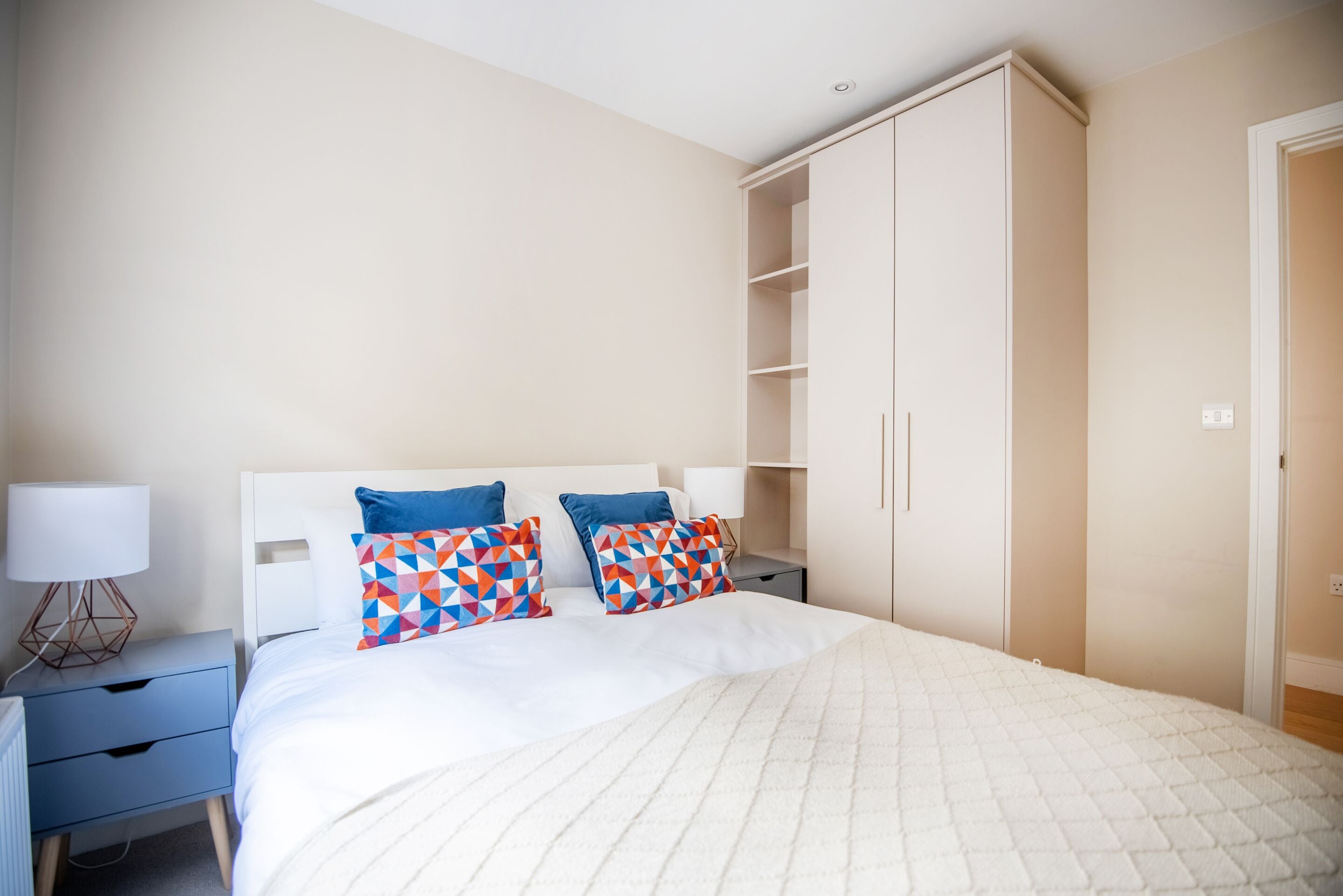 Un dormitorio con cama, dos mesitas de noche, un armario y una lámpara de noche.