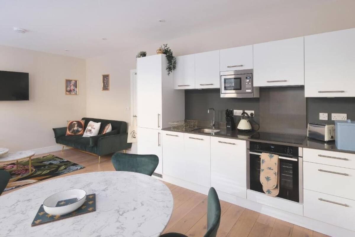Una cocina moderna con armarios blancos, un microondas y un lavavajillas. Hay una zona de comedor con una mesa redonda y sillas.