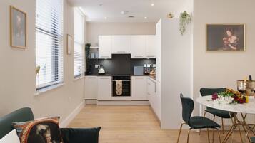 A modern kitchen with white cabinets, a black oven, and a dining area with a white table and green chairs.