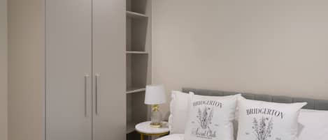 A bedroom with a bed, white pillows, a nightstand, a lamp, and a wardrobe.