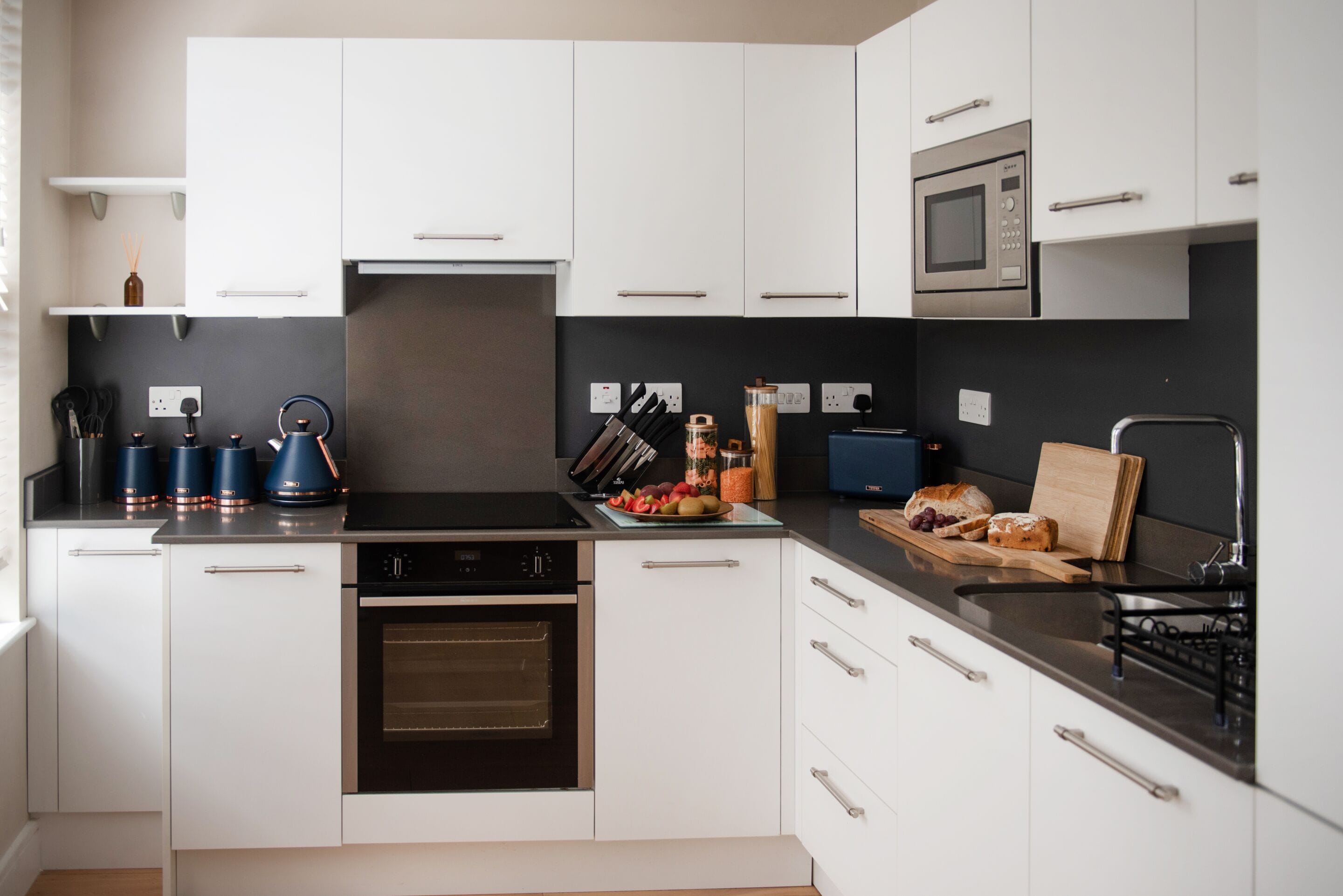 Eine moderne Küche mit weißen Schränken, einer schwarzen Arbeitsplatte und Edelstahlgeräten, darunter eine Mikrowelle und ein Backofen.